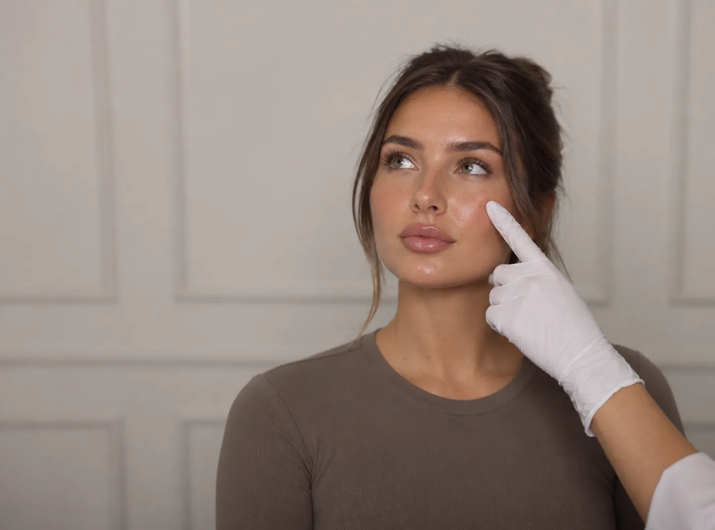 A practitioner in a white glove points to a client's cheekbone during a skin consultation