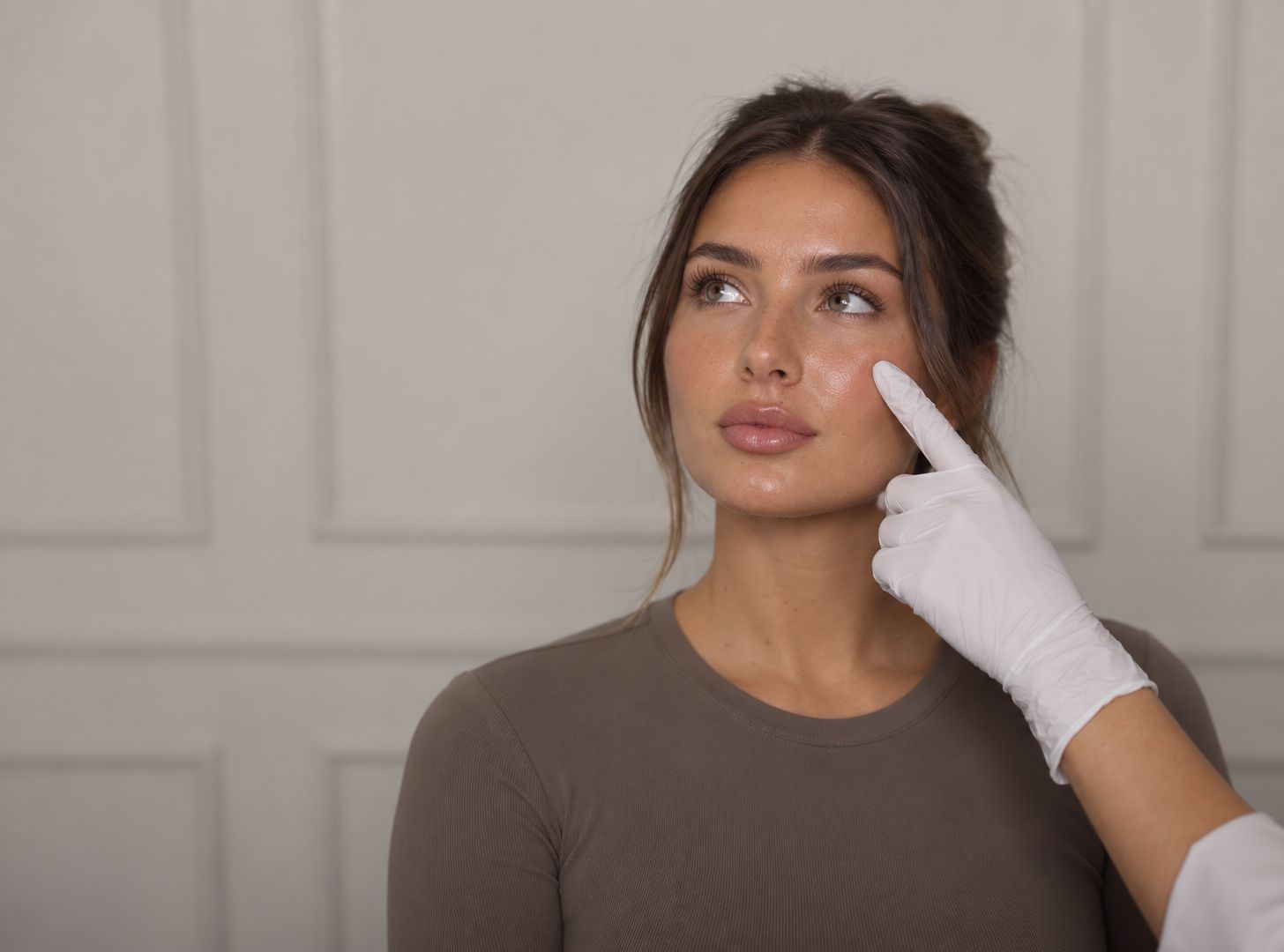 A practitioner in a white glove points to a client's cheekbone during a skin consultation